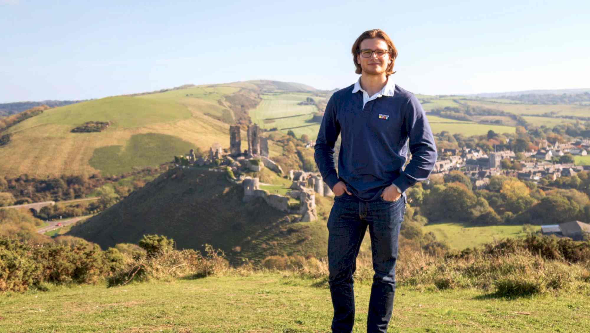 Young man standing on a hill overlooking Corfe Castle, Dorset, England